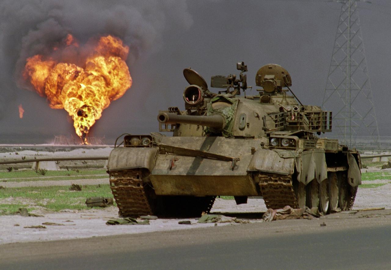 Das Wrack eines verlassenen irakischen Panzers vom typ T-62 sowjetischer Bauart steht am 02.04.1991 am Rande einer Wüstenstrasse in Kuwait während im Hintergrund ein brennendes Bohrloch des Al-Ahmadi Ölfeldes zu sehen ist. (Archivbild) 