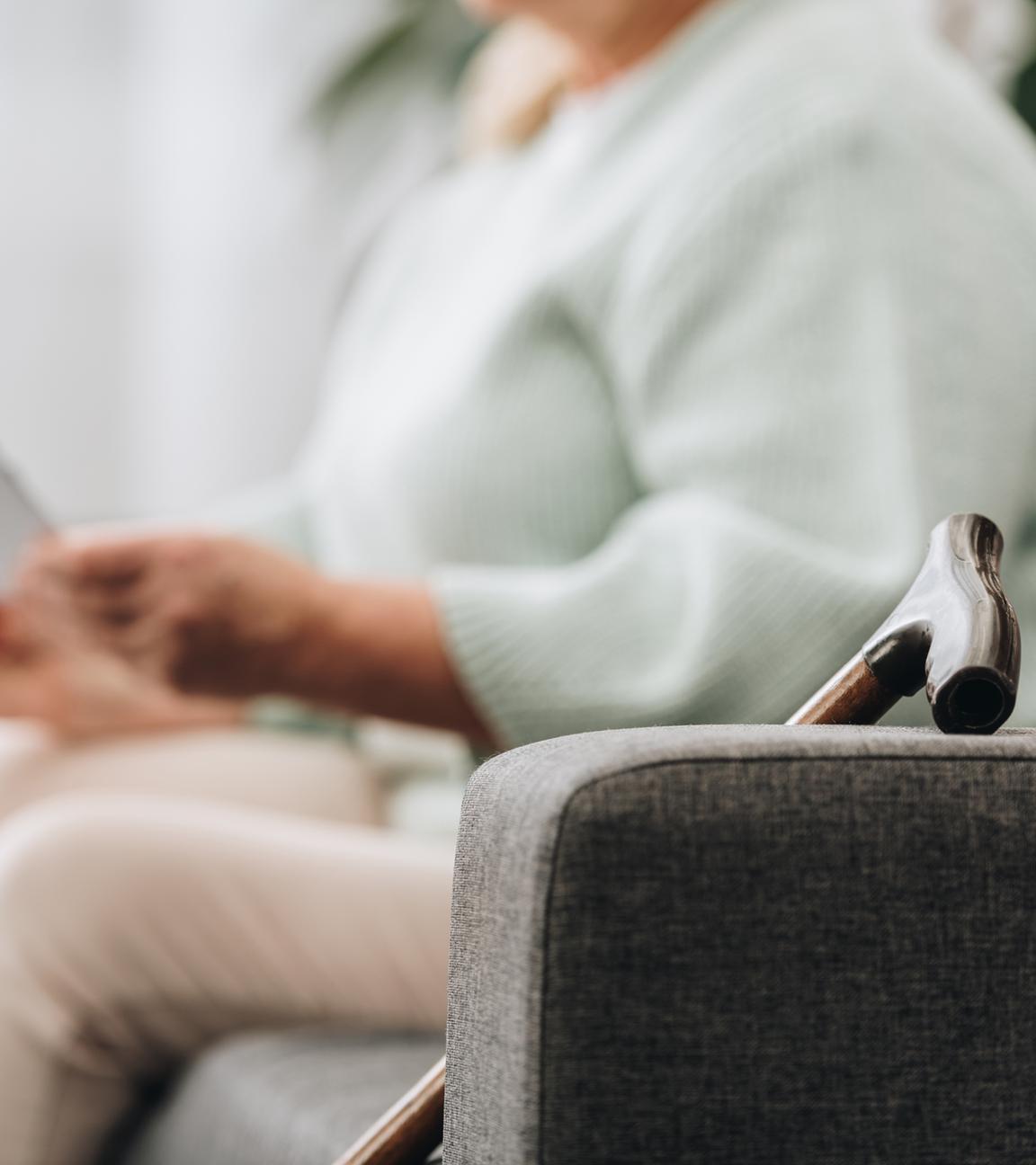 Eine ältere Frau sitzt mit Gehstock auf dem Sofa und liest einen Brief.