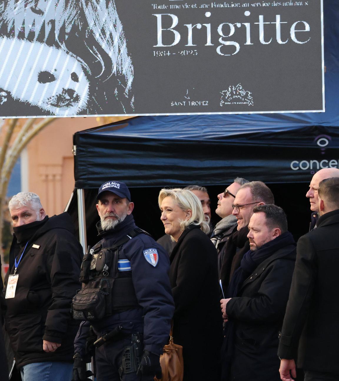 Mehrere Personen, darunter Marine Le Pen sowie Polizisten, in überwiegend schwarzer Kleidung. Über ihnen eine Art Plakat mit der Aufschrift "Brigitte".