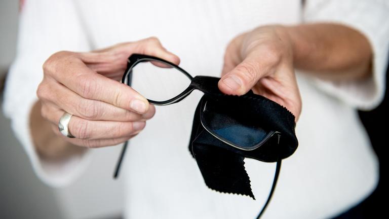 Es ist eine Person zu sehen, wie sie gerade ihre Brille mit einem Tuch putzt.