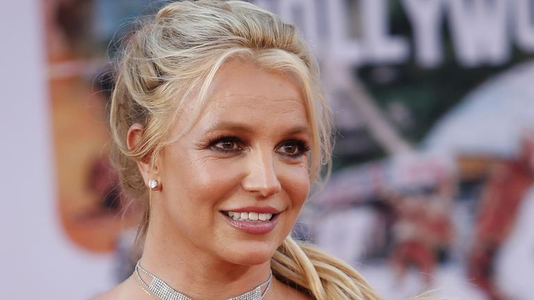 Britney Spears lächelt in einem roten Kleid in die Kamera