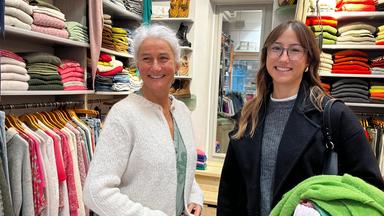 Britta und ihre Tochter Marisa stehen in einer Boutique in Eckernförde vor Regalen mit Bekleidung. Beide schauen lächelnd nach vorne.