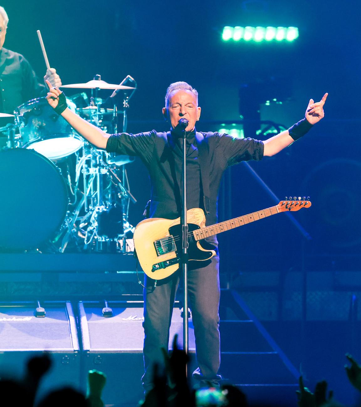 Bruce Springsteen gibt ein Konzert und hält seine Hände in die Höhe.