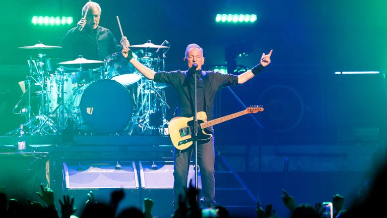 Bruce Springsteen gibt ein Konzert und hält seine Hände in die Höhe.
