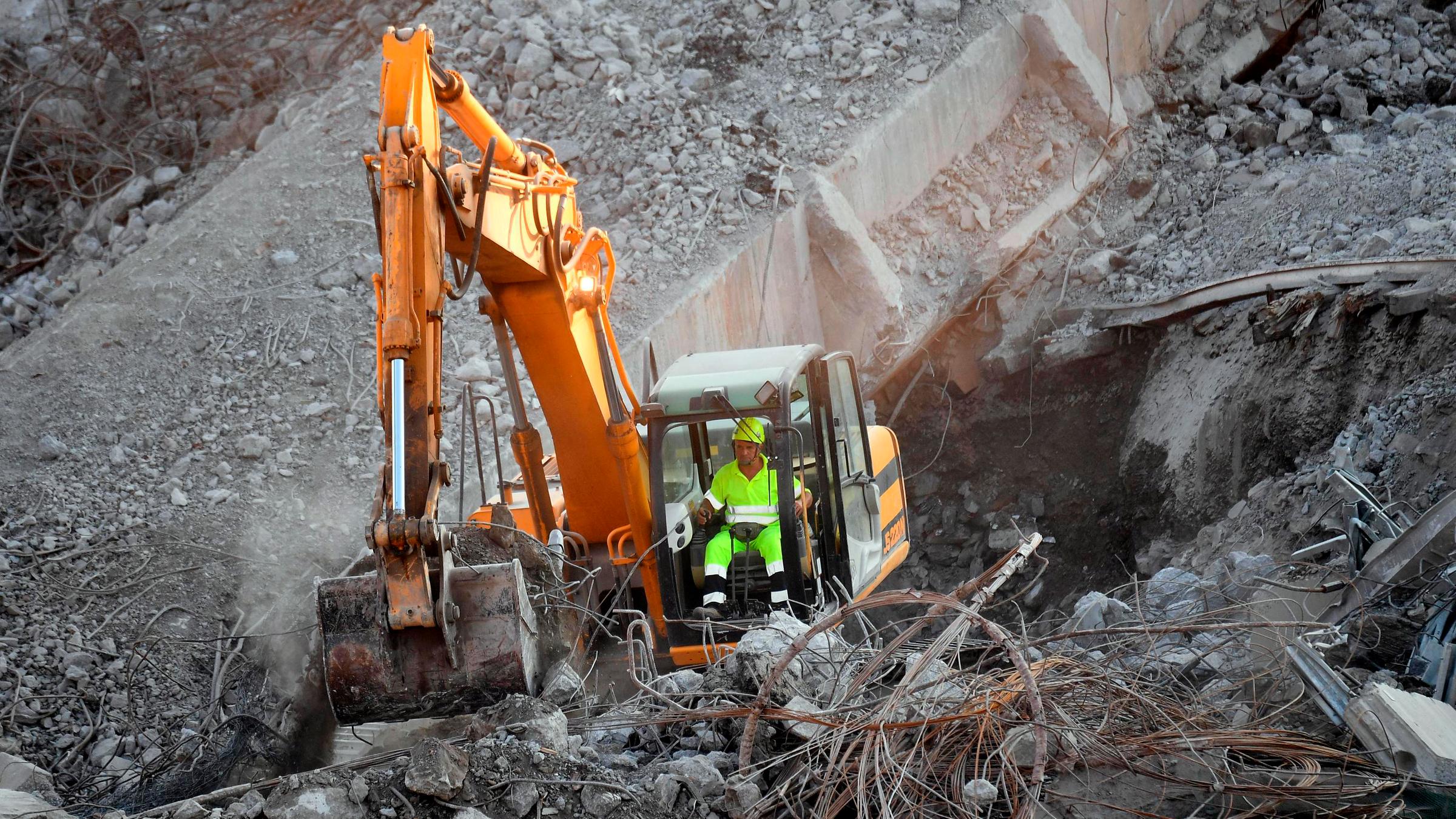 Ein Baggerfahrer entfernt mit seinem Bagger Trümmer der Autobahnbrücke in Genua