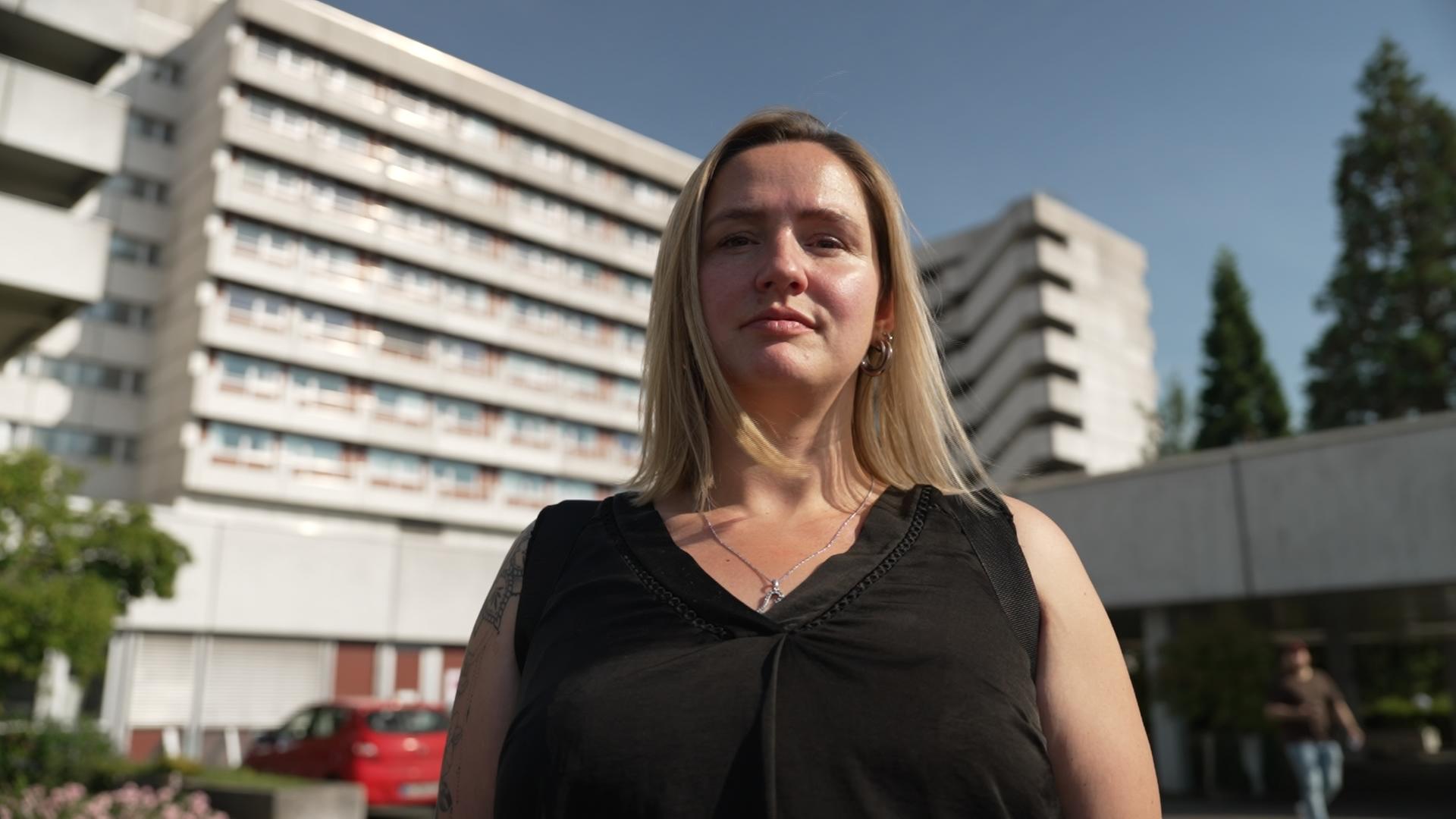 Brustkrebspatientin Jacqueline steht vor einer Klinik.
