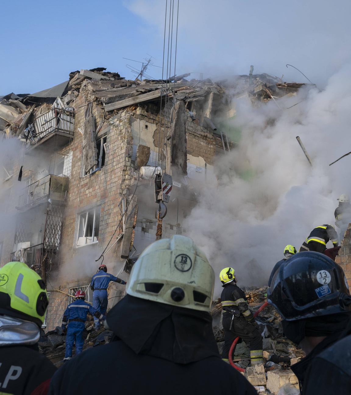 Im Hintergrund ist ein verschüttetes Gebäude aus dem Rauch kommt. Im Vordergrund sind Feuerwehrmänner