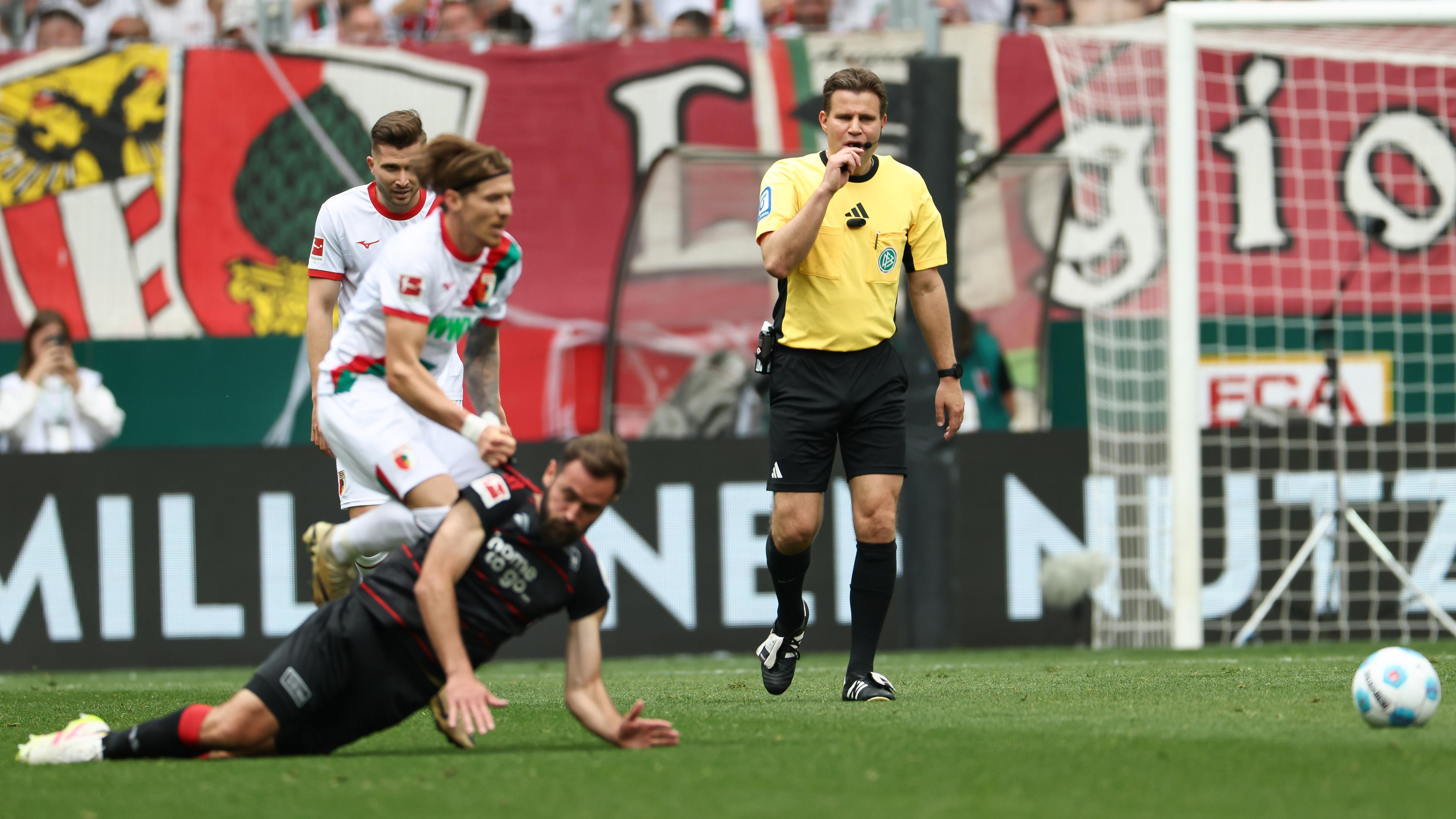 Schiedsrichter Felix Brych (r) pfeifft das Foul von Kristijan Jakic von FC Augsburg (l) an Lucas Toussart von Union Berlin ab.