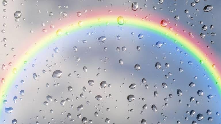 Regenbogen hinter einer Scheibe mit Regentropfen