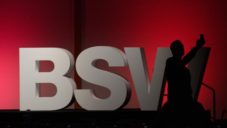 Ein Teilnehmer des 3. Bundesparteitages vom BSW steht vor großen Lettern die auf der Bühne des Parteitages stehen und fotografiert.