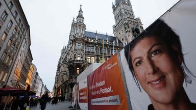 Menschen gehen an Plakaten vorbei, auf denen eine Wahlkampfveranstaltung mit der Vorsitzenden des linkspopulistischen Bündnisses Sahra Wagenknecht (BSW) angekündigt wird. Sahra Wagenknecht startet am 3. Februar 2025 auf dem zentralen Marienplatz in München den Wahlkampf der Partei.