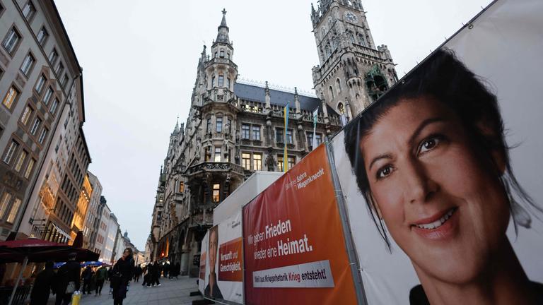 Menschen gehen an Plakaten vorbei, auf denen eine Wahlkampfveranstaltung mit der Vorsitzenden des linkspopulistischen Bündnisses Sahra Wagenknecht (BSW) angekündigt wird. Sahra Wagenknecht startet am 3. Februar 2025 auf dem zentralen Marienplatz in München den Wahlkampf der Partei.