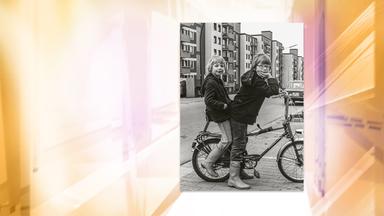 Auf einer Schwarz-Weiß-Fotografie sieht man zwei Jungen auf einem Bonanzarad. Im Hintergrund befinden sich Wohngebäude.