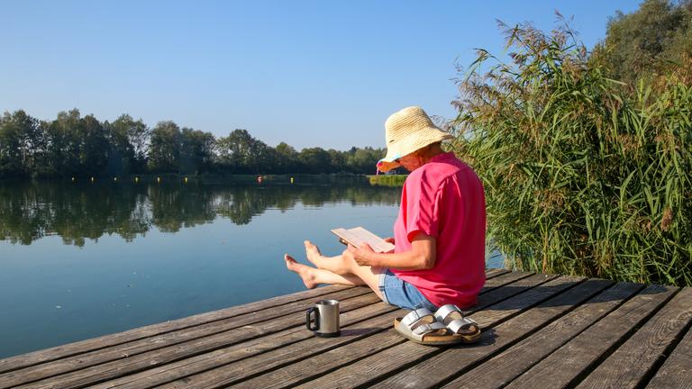 Eine Frau liest ein Buch auf einer Badeplattform an einem See.