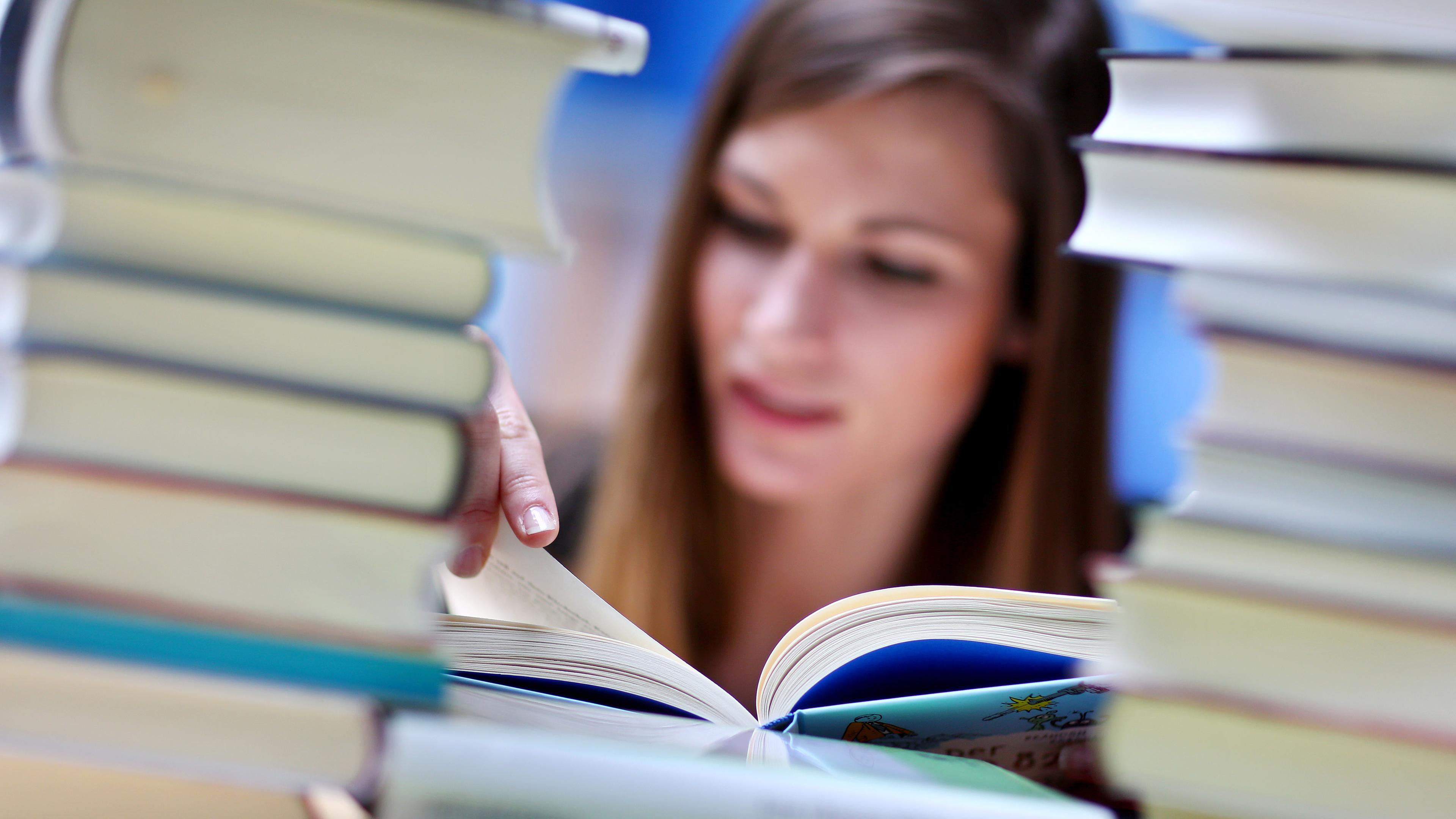Frau liest hinter Bücherstapel
