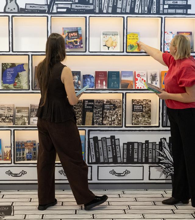 Zwei Frauen räumen ein Bücherregal ein, das wie ein gemalter Bücherschrank aussieht.