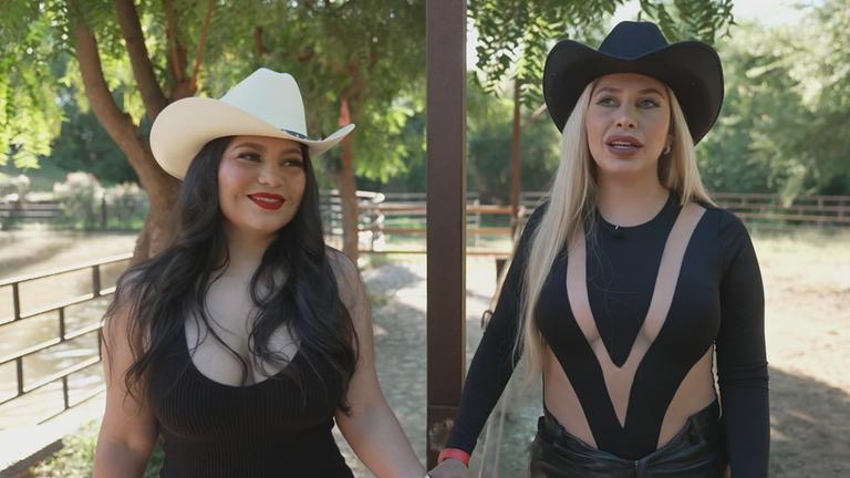 Zwei Frauen laufen Hand in Hand auf einer Ranch entlang.