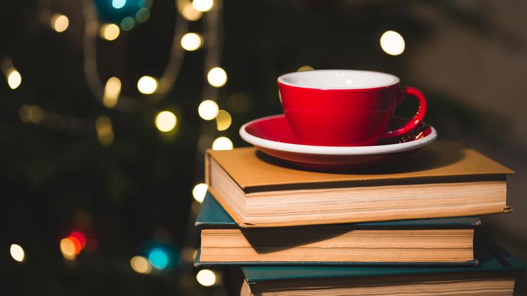 Teetasse auf einem Bücherstapel, im Hintergrund unscharf ein geschmückter Weihnachtsbaum.