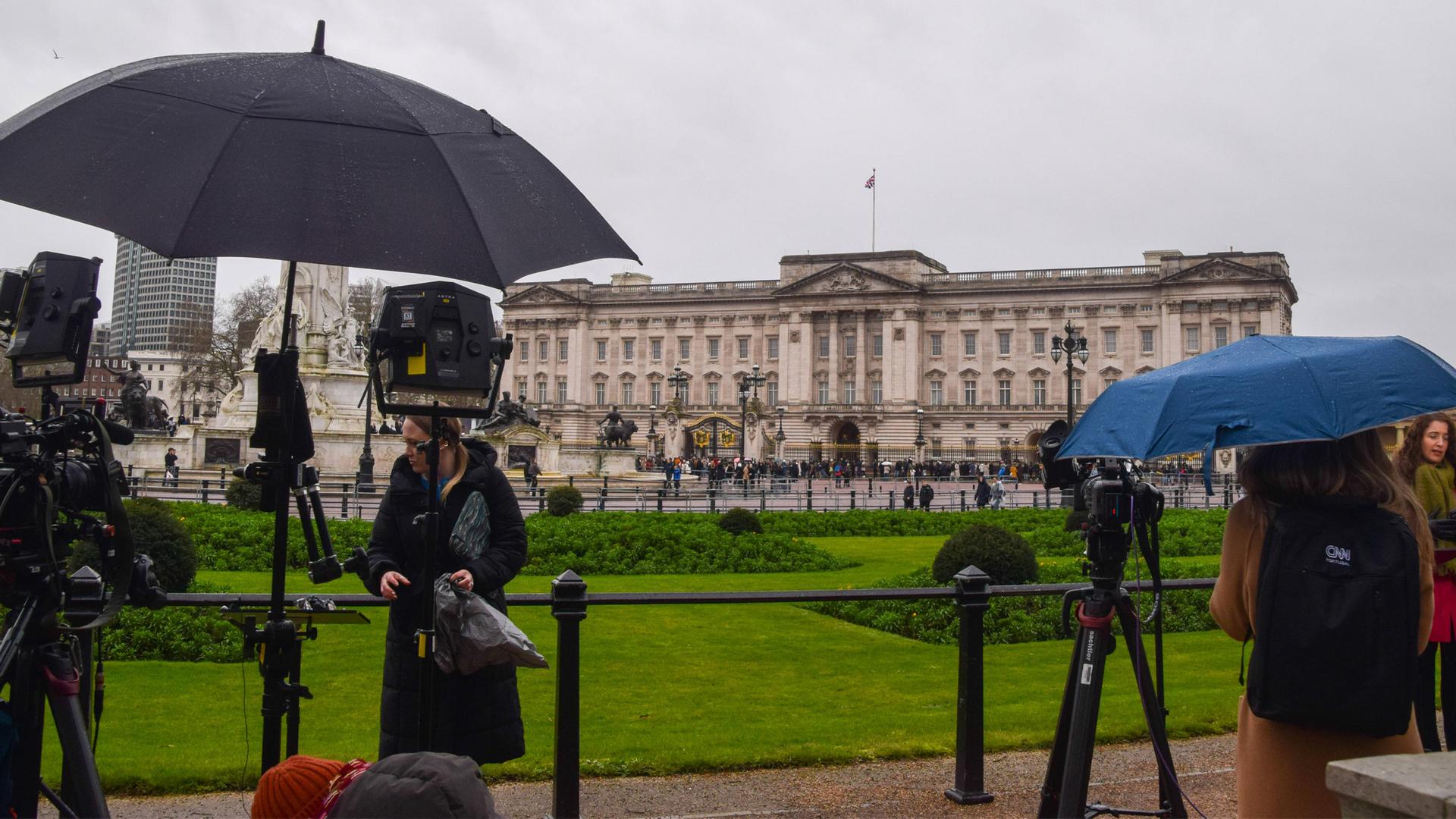 Pressevertreter versammeln sich mit Schirmen vor dem Buckingham Palace am 20.02.2026.