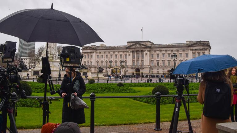 Pressevertreter versammeln sich mit Schirmen vor dem Buckingham Palace am 20.02.2026.