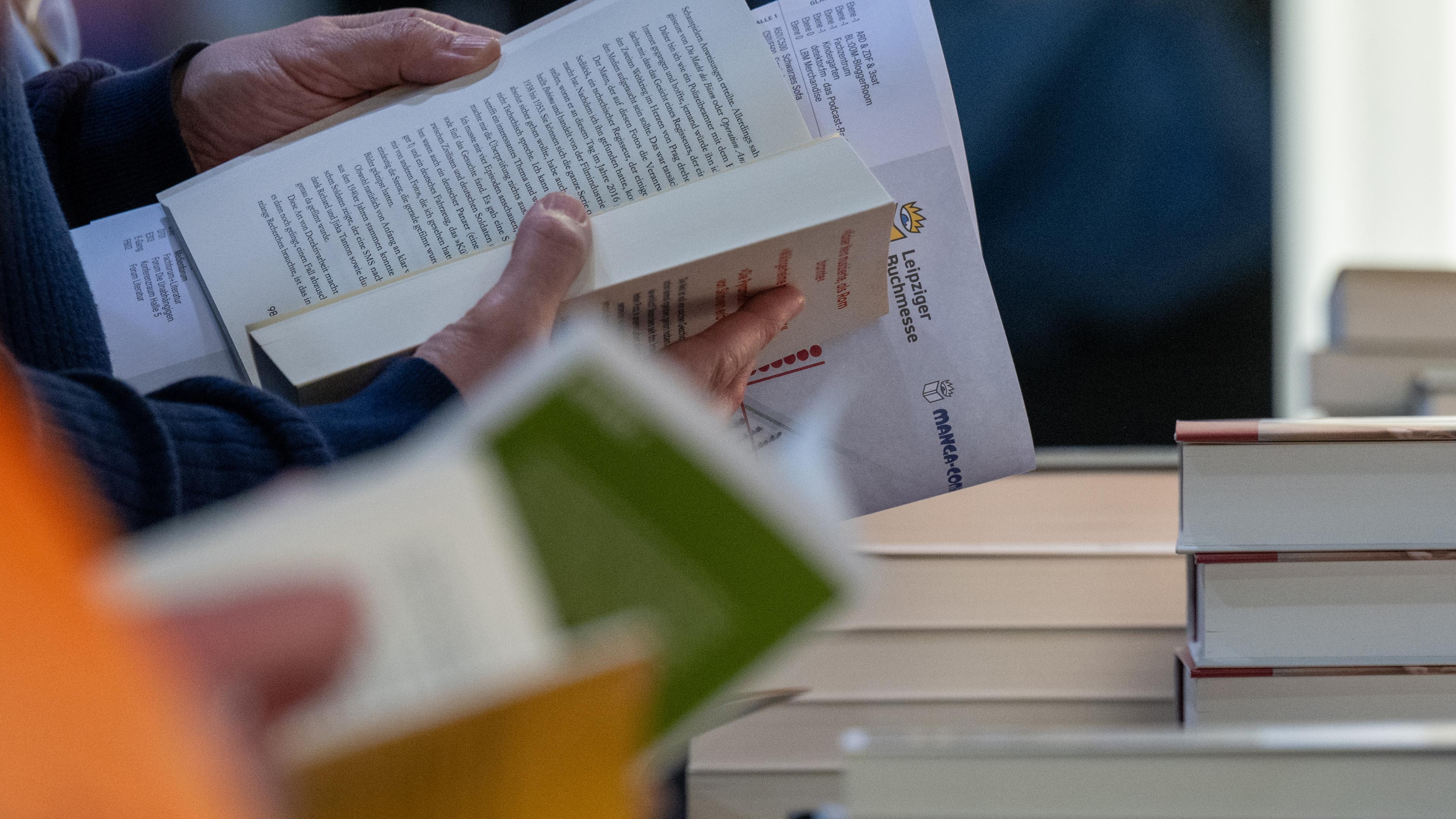 Besucher einer Buchmesse lesen an einem Stand.