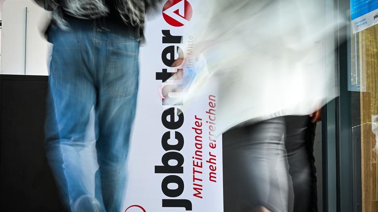 Personen gehen am Logo vom Jobcenter Berlin-Mitte bei der Jobmesse am 25.06.2025 vorbei. 