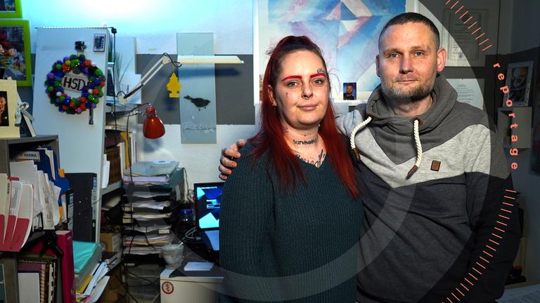 Nadine und Ronny schauen Arm in Arm frontal in die Kamera.