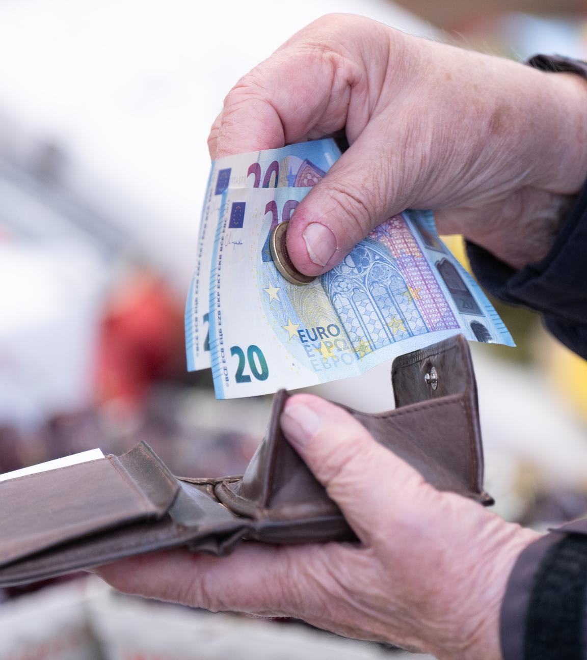 Eine Frau sortiert auf einem Wochenmarkt das Wechselgeld für ihre Einkäufe in ein Portemonnaie.
