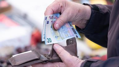 Eine Frau sortiert auf einem Wochenmarkt das Wechselgeld für ihre Einkäufe in ein Portemonnaie.
