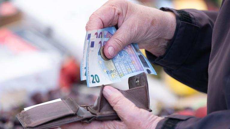 Eine Frau sortiert auf einem Wochenmarkt das Wechselgeld für ihre Einkäufe in ein Portemonnaie.