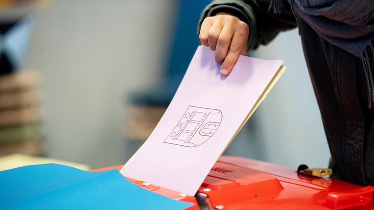 Ein Wahlzettel wird in eine Wahlurne gesteckt.