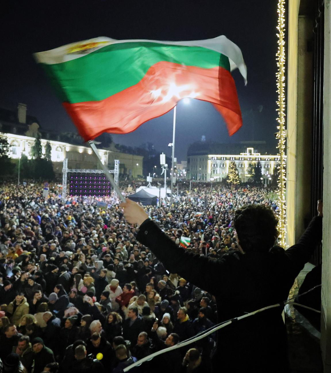 Ein Student schwenkt bei Dunkelheit eine bulgarische Flagge, während eine anschwellende Menge von Zehntausenden von Bulgaren den zentralen Platz in Sofia füll