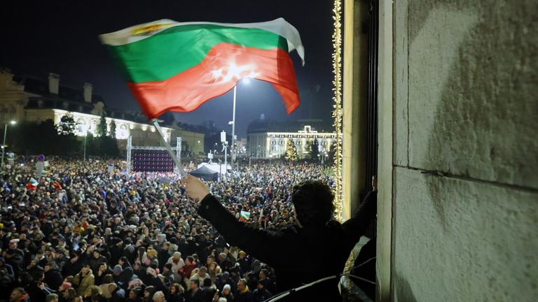 Ein Student schwenkt bei Dunkelheit eine bulgarische Flagge, während eine anschwellende Menge von Zehntausenden von Bulgaren den zentralen Platz in Sofia füll