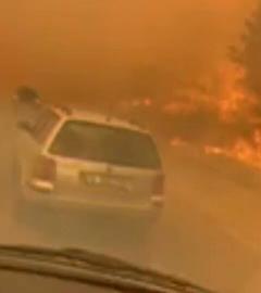 Ein Auto steht auf einer Autobahn, direkt neben einem Waldbrand, der alles in rot-oranges Licht taucht.