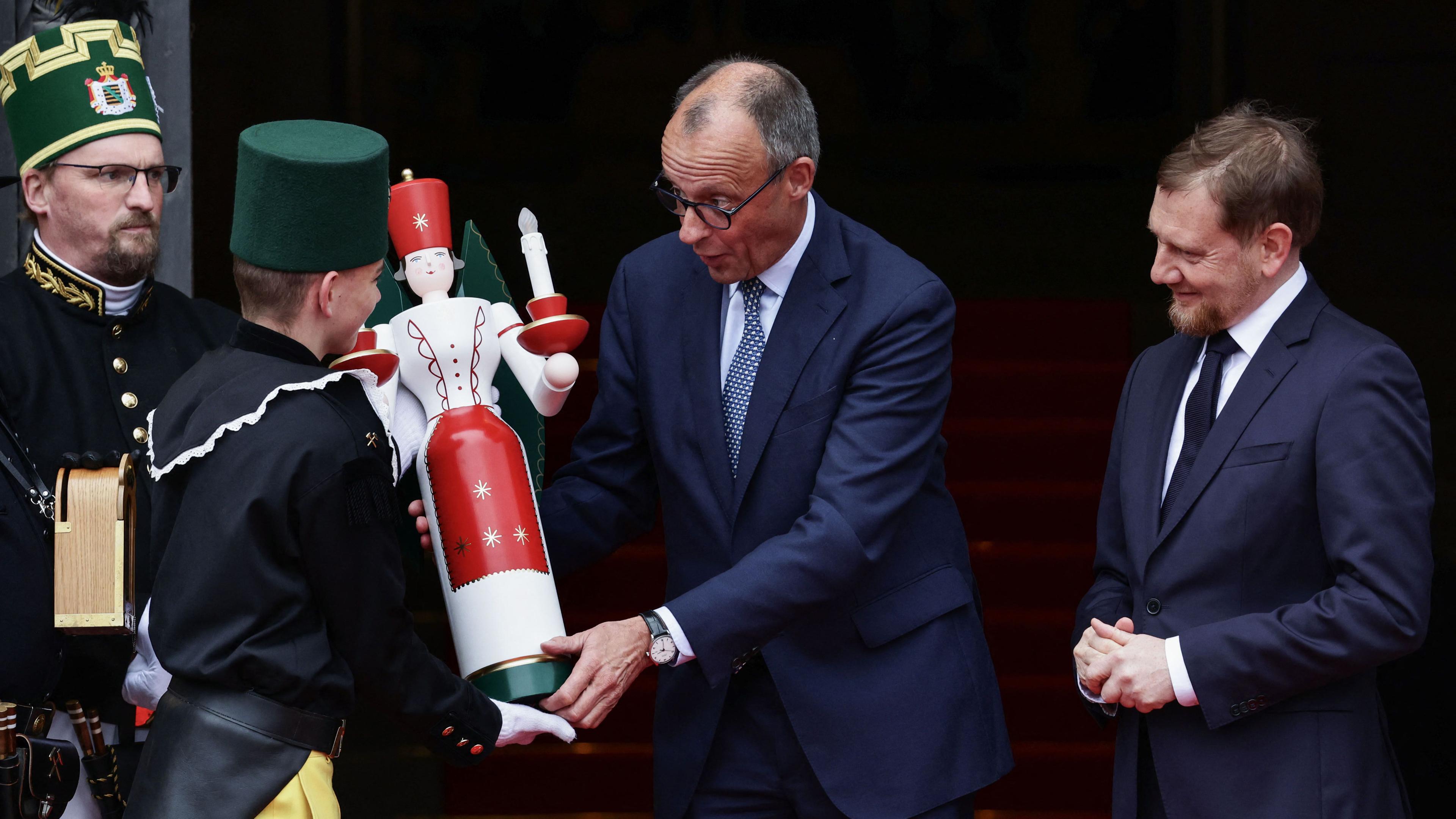 Sachsen, Dresden: Bundeskanzler Friedrich Merz (Mitte) erhält vom Bergmannsmusikkorps einen traditionellen hölzernen Kerzenständer überreicht