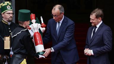 Sachsen, Dresden: Bundeskanzler Friedrich Merz (Mitte) erhält vom Bergmannsmusikkorps einen traditionellen hölzernen Kerzenständer überreicht