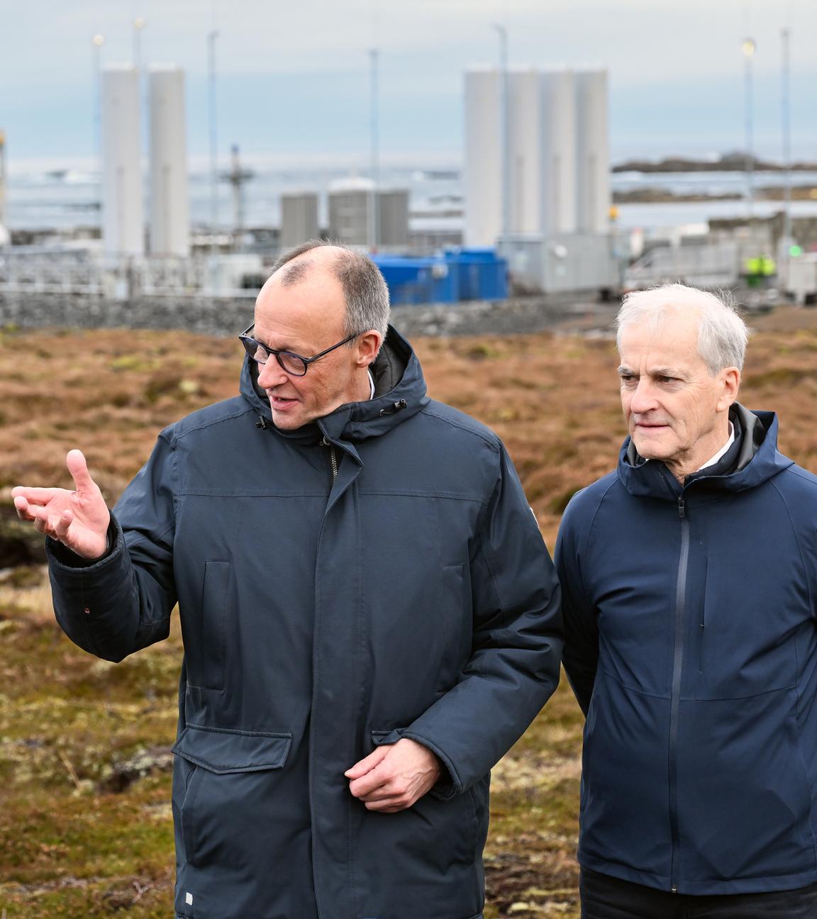 Norwegen, Andenes: Bundeskanzler Friedrich Merz (l, CDU) und Jonas Gahr Støre, Ministerpräsident von Norwegen, unterhalten sich vor der Kulisse der Raketenstartrampe (l) im Andoya Space Port. 