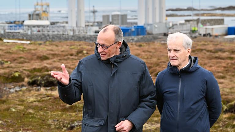 Norwegen, Andenes: Bundeskanzler Friedrich Merz (l, CDU) und Jonas Gahr Støre, Ministerpräsident von Norwegen, unterhalten sich vor der Kulisse der Raketenstartrampe (l) im Andoya Space Port. 