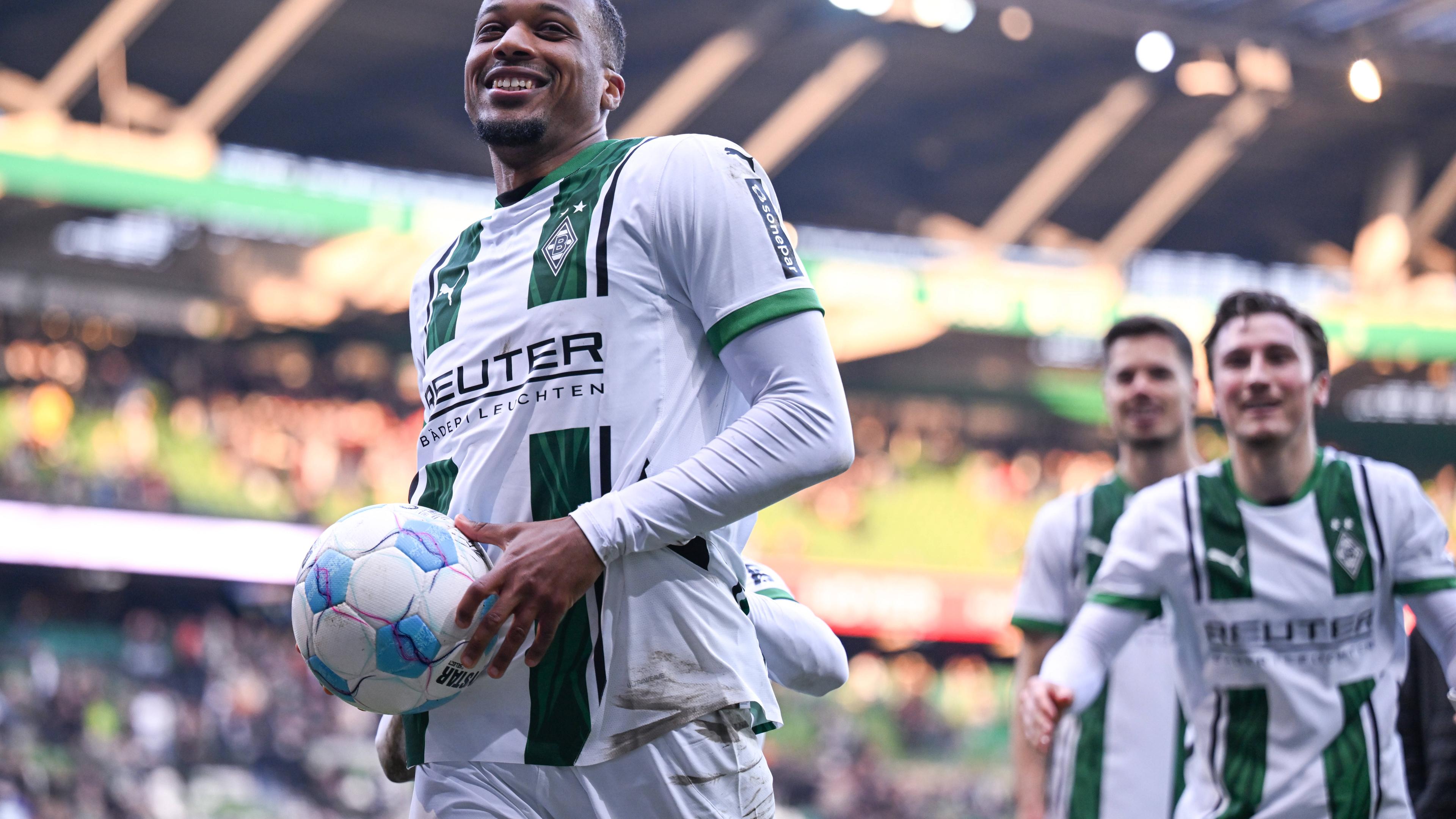 Gladbachs Alassane Plea feiert mit den Fans den Auswärtssieg und hält den Spielball fest.