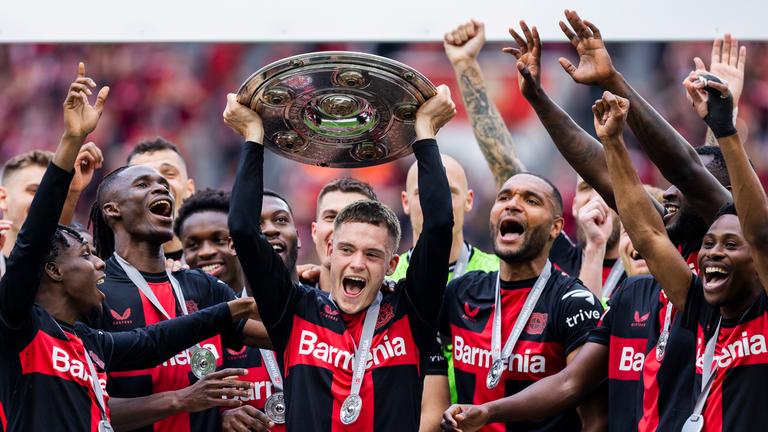 Florian Wirtz streckt die Meisterschale, umjubelkt von seinen Mannschaftskollegen des Bayer 04 Leverkusens, hoch.