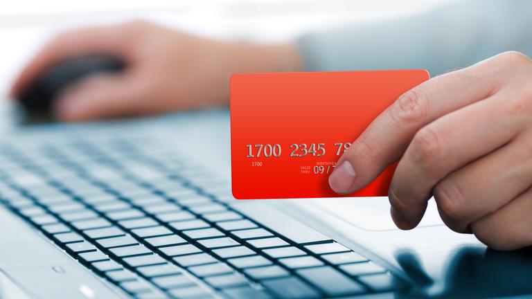Mann hält eine Kreditkarte in der Hand und ist nebenbei am Laptop.