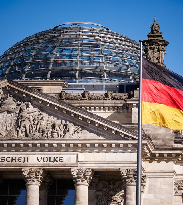 Das Gebäude des deutschen Bundestages.Im Vordergurnd weht eine deutsche Flagge. 