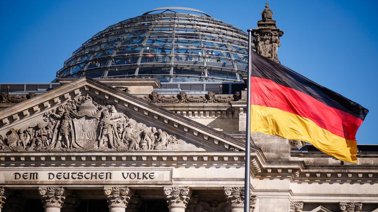 Das Gebäude des deutschen Bundestages.Im Vordergurnd weht eine deutsche Flagge. 