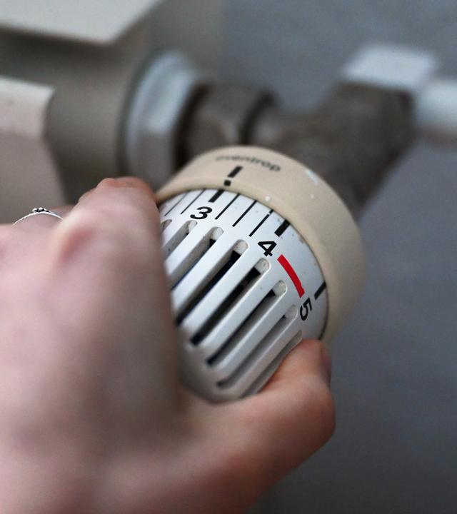24.02.2026, Berlin: Eine Frau dreht an einem Thermostatregler einer Heizung in einer Wohnung.