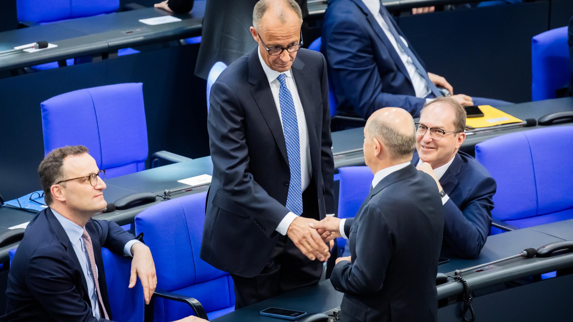Berlin: Der designierte Bundeskanzler Friedrich Merz (CDU, M oben) und der geschäftsführende Bundeskanzler Olaf Scholz (SPD, unten M) schütteln sich neben Jens Spahn (CDU, l), Vorsitzender der CDU/CSU Bundestagsfraktion, und Alexander Dobrindt (CSU, r), designierter Innenminister, im Bundestag beim zweiten Durchgang der Kanzlerwahl die Hand.