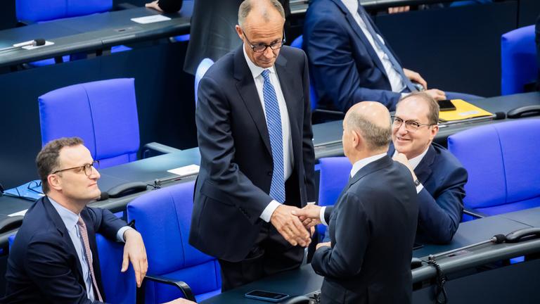 Berlin: Der designierte Bundeskanzler Friedrich Merz (CDU, M oben) und der geschäftsführende Bundeskanzler Olaf Scholz (SPD, unten M) schütteln sich neben Jens Spahn (CDU, l), Vorsitzender der CDU/CSU Bundestagsfraktion, und Alexander Dobrindt (CSU, r), designierter Innenminister, im Bundestag beim zweiten Durchgang der Kanzlerwahl die Hand.
