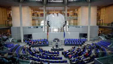 Deutscher Bundestag. Vogelperspektive des Saals. Der Bundesadler und einige Abgeordneten sind zu sehen.
