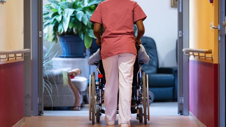 Eine Bewohnerin eines Pflegeheims wird von einer Pflegerin einen Gang entlang geschoben.