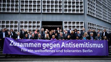 Zahlreiche Gäste stehen mit einem Banner mit der Aufschrift «Zusammen gegen Antisemitismus - Für ein weltoffenes und tolerantes Berlin» vor der Kaiser-Wilhelm-Gedächtniskirche bei der zentralen Gedenkveranstaltung zum Jahrestag des Hamas-Angriffs auf Israel vom 7. Oktober 2023.