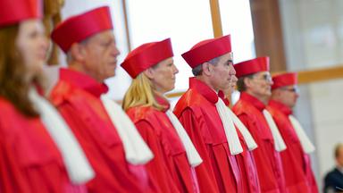Männer und Frauen stehen in den Roben des Bundesverfassungsgerichtes hinter ihrem Richterstand. 